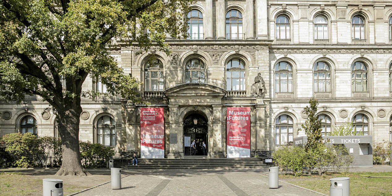 Außenansicht des Museums für Naturkunde Berlin; links und rechts vom Eingang die Banner, rot und weiß, vom Martin Roth Symposium