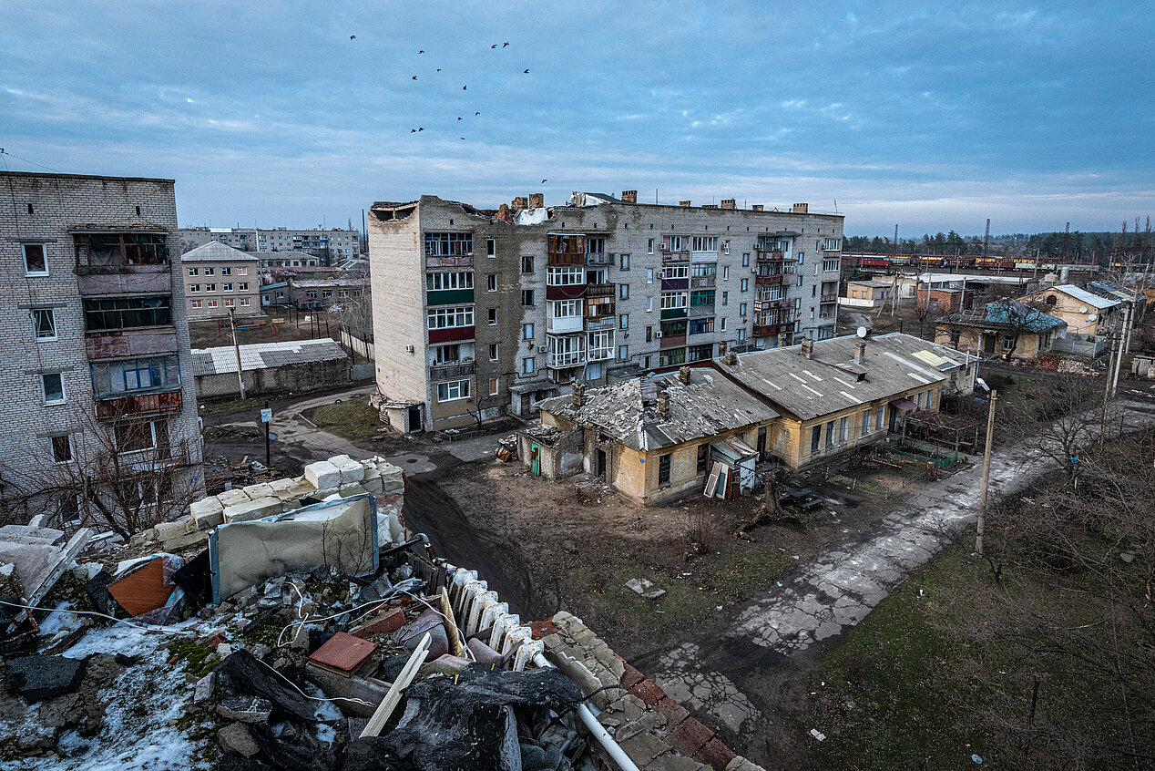 You can see a photo of an apartment building block in Ukraine. The sky is clear, and there’s some grass in the foreground. The buildings, however, are destroyed. The armed aggression of Russia destroyed them.