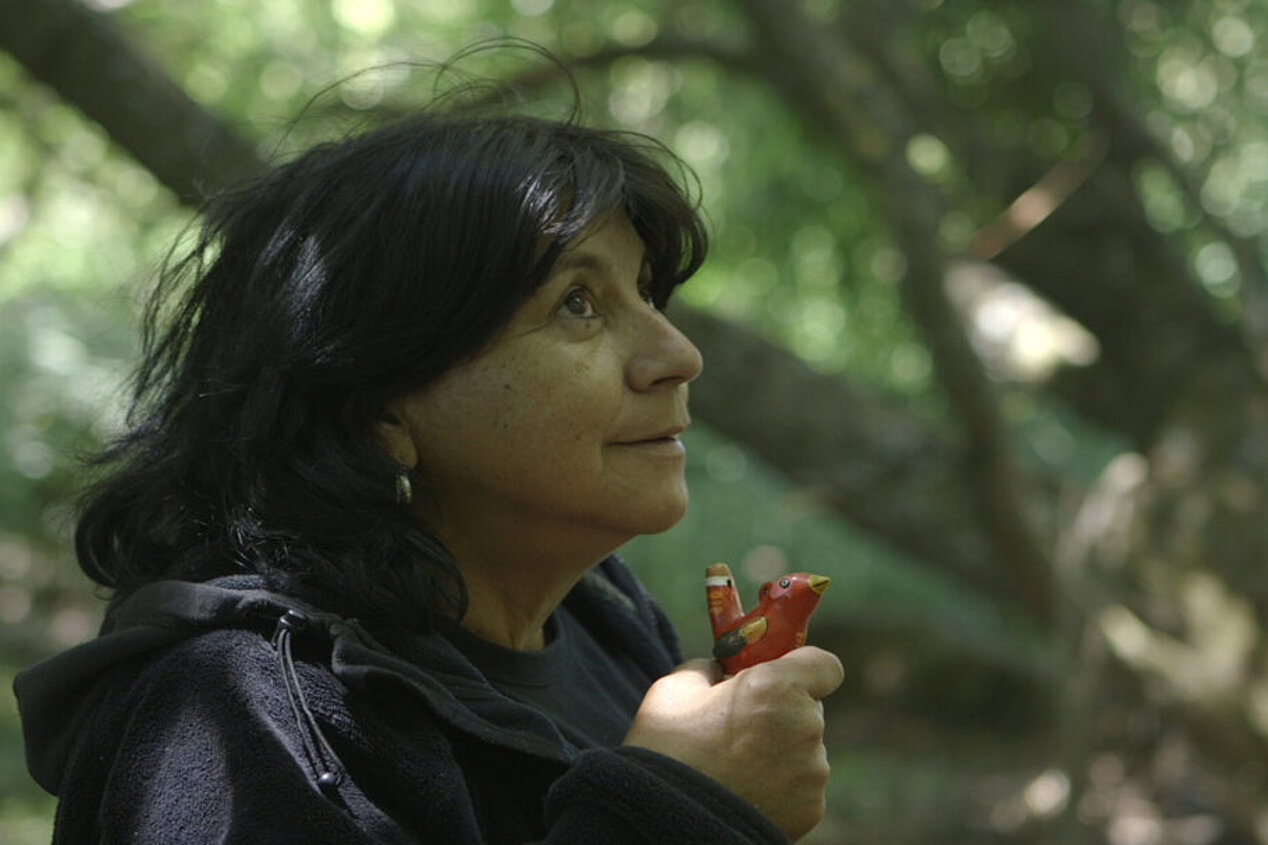 Eine Frau mit dunklen schulterlangen Haaren hält eine bunte Vogelpfeife in ihrer Hand.