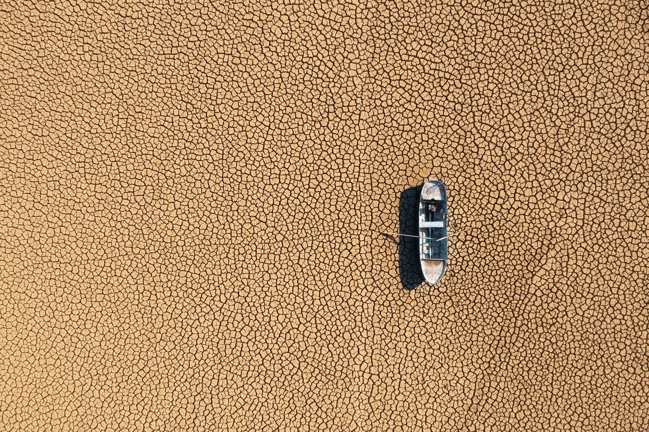  The photo shows a small, lonely boat in the middle of a dry lakebed.