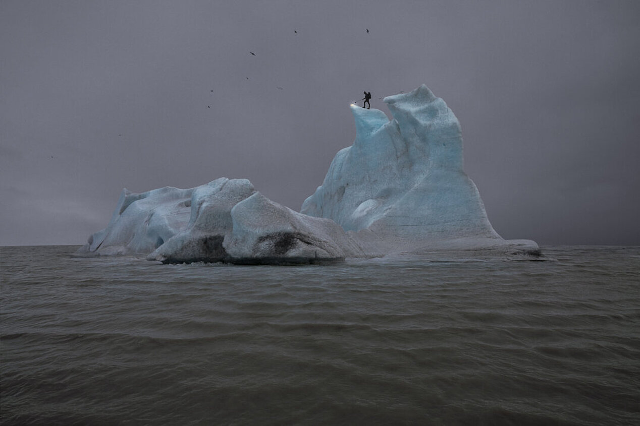 Ein Eisblock im Meer mit einer Person, die auf einer Spitze des Eisbergs steht.