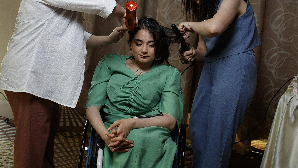 Jamila Mammadli, a model sitting in a wheelchair, gets her hair and makeup done by two women. Photograph: Ismayil Fataliyev