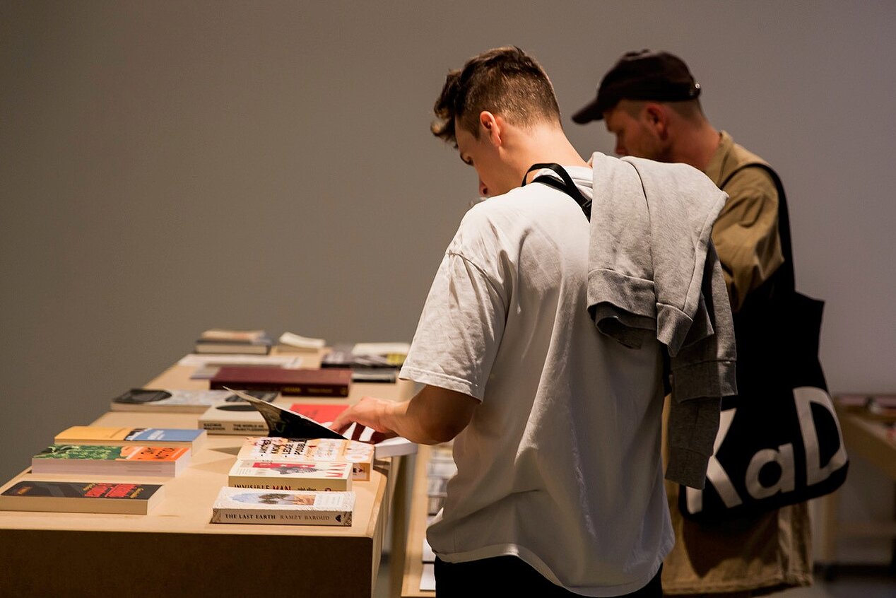 Besucher einer Ausstellung blättern durch Kataloge