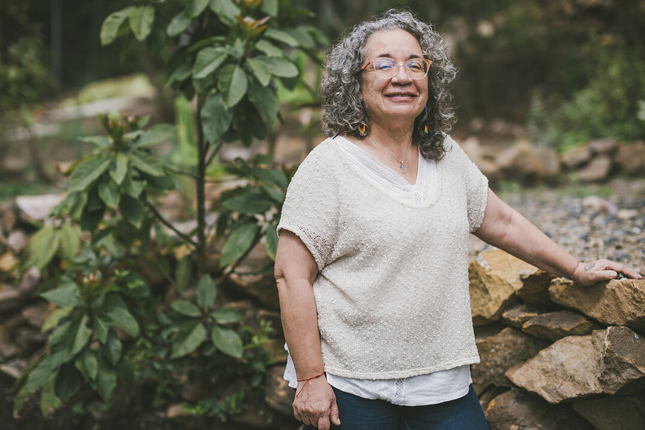 Die kolumbianische Aktivistin Rosa Emilia Salamanca steht in ihrem Garten vor einer Steinmauer. als ein Säen von Samen, aus denen einmal ein Wald wächst