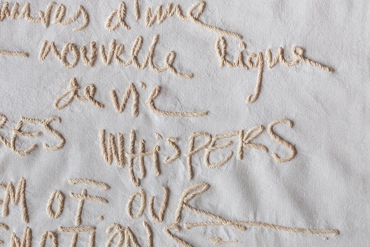 You can see a close-up of Joël Andrianomearisoa's MEASURES LULLABIES AND WHISPERS. The colors are beige, it is an embroidered fabric, you can see the words Nouvelle and Whispers, for example.