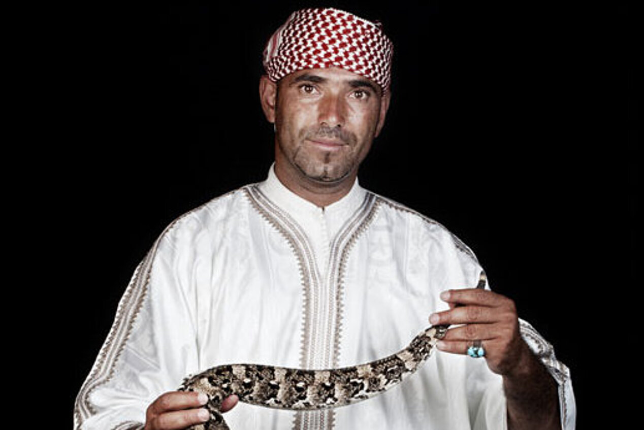 Fotografie eines Mannes vor schwarzem Hintergrund, der eine Schlange in seinen Händen hält
