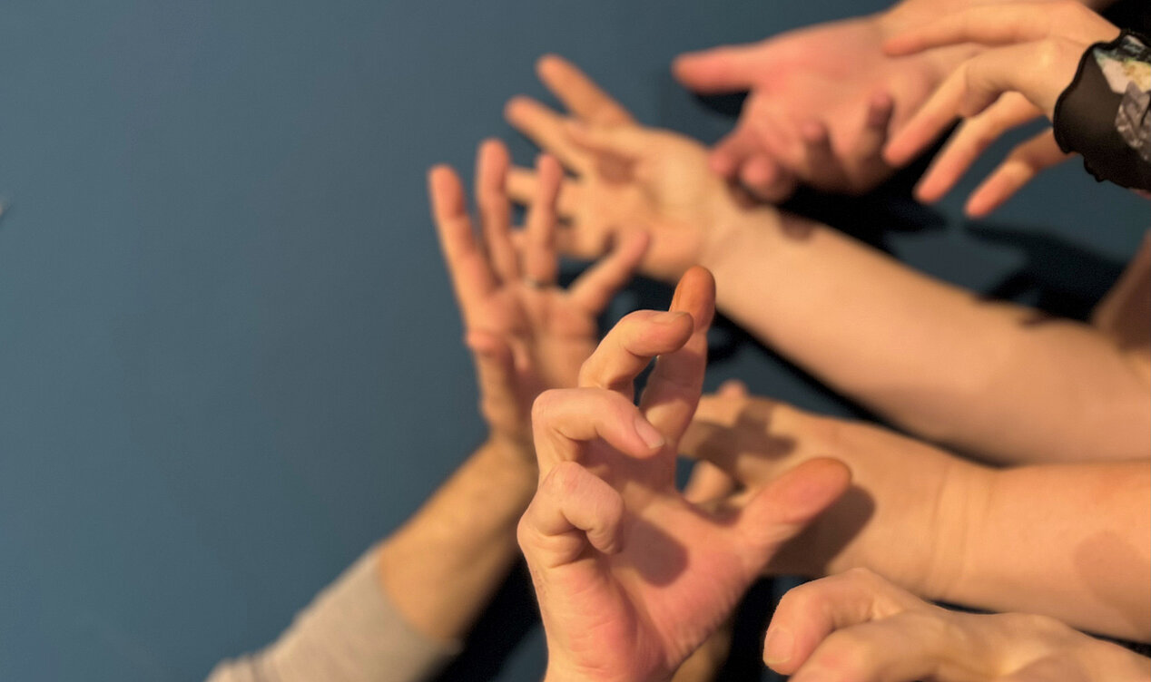 Auf dem Bild sind ausgestreckte, miteinander verwobene Hände zu sehen, vor einem blauen Hintergrund. Es handelt sich um das Titelbild zum Workshop Bewegungsreise im Rahmen der Ausstellung Camila Sposati – Atem-Stücke in der ifa-Galerie Stuttgart. 