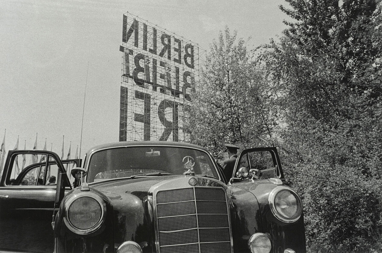 A car in front, behind it trees, flags and a sign