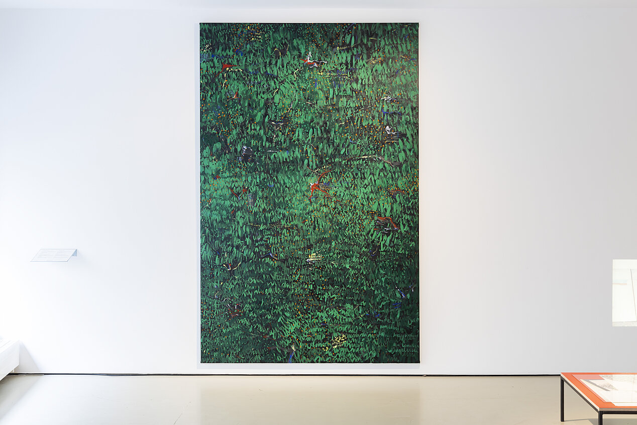 You can see an exhibition view in the photo. It is a painting on a white wall. The painting is by Lizza May Davis and has green colors with a few dabs of red. It looks like a view of a forest.