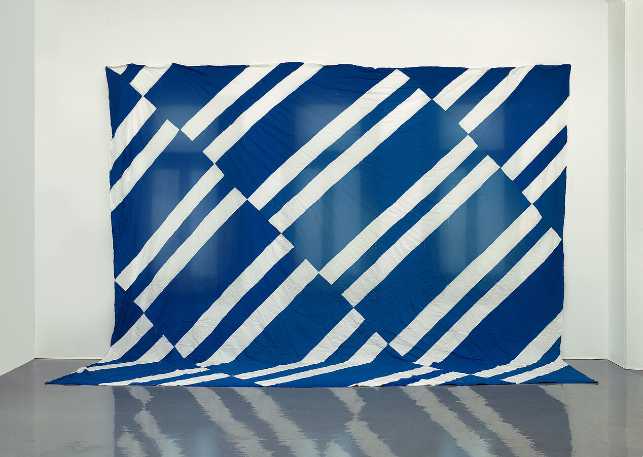 You see a fabric installation that resembles a curtain on a white wall. It is blue with white stripes.