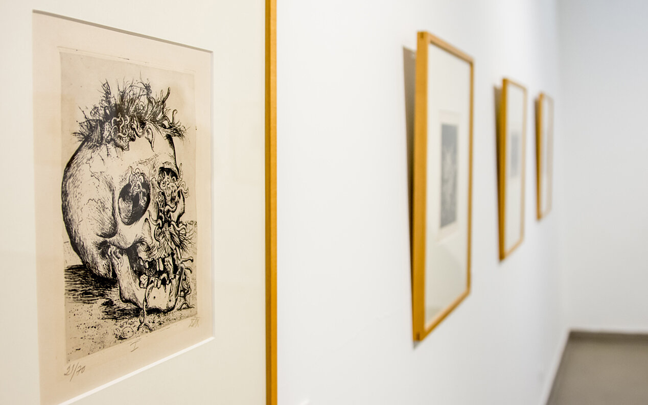 Four pictures in a wooden frame can be seen hanging on a white wall. At the very front is an etching of a skull. These are works by the German painter and graphic artist Otto Dix, whose works were mainly known for their Realism and Neue Sachlichkeit (New Objectivity). Photo: Goethe-Institut Karachi / Humayun Memon  