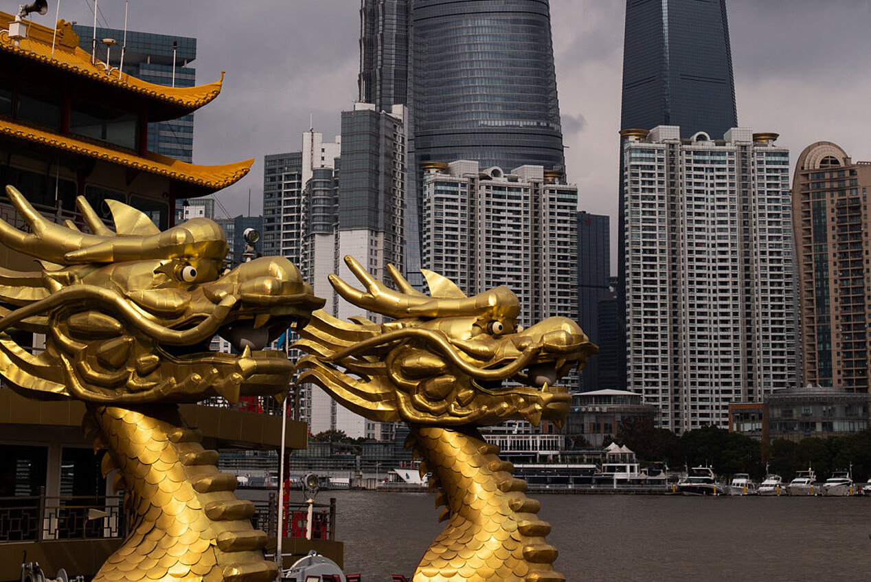 Zwei goldene Drachenskulpturen und Teile eines traditionellen chinesischen Bauwerkes vor Hochhäusern